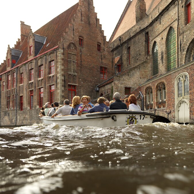 Boat with visitors on the canal in Bruges, surrounded by medieval brick houses. | ©  Visit Bruges – Boat trip