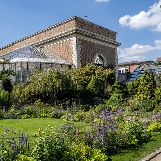 Blühender botanischer Garten in Leuven mit gepflegten Blumenbeeten, Grünflächen und einem historischen Gewächshaus aus Backstein und Glas bei sonnigem Wetter. | © Stad Leuven, Jan Crab