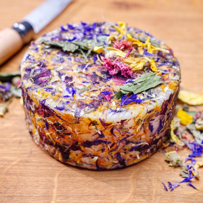 Traditioneller Alpenkäse mit Kräuterblumen der Alpen, angeboten als Laib in Österreich | © shutterstock / 2337113239