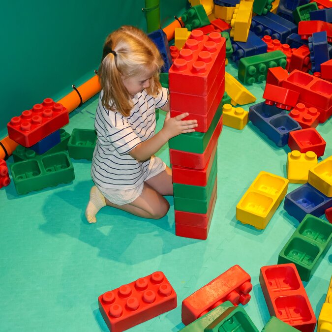A girl plays on the floor with different coloured Lego bricks. | © shutterstock / 2503988239