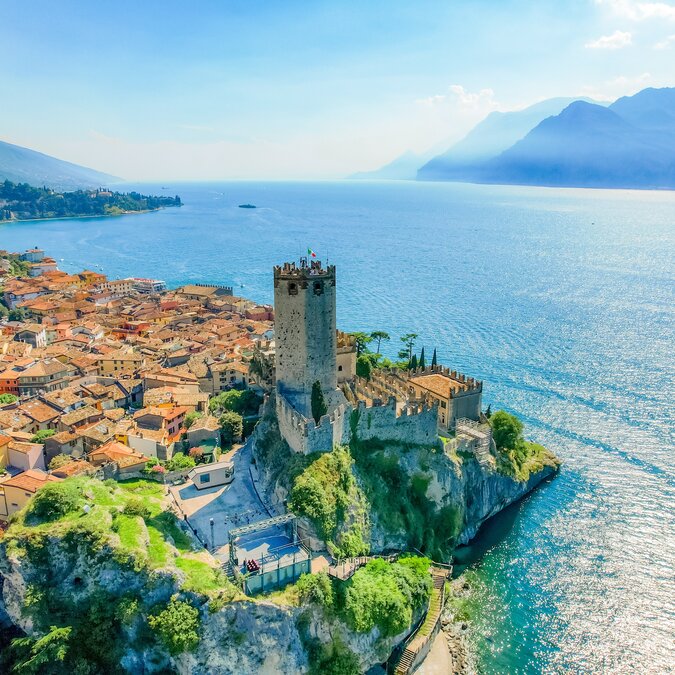 Aerial view of Scalinger Castle and the old town centre of Malcesine directly on the shore of Lake Garda and mountains in the background | © shutterstock / 2498491379