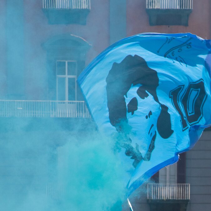Flagge mit Maradonna und blauer Dunst bei einem Strassenzug vor einem Fussballspiel | © shutterstock / 2309064385